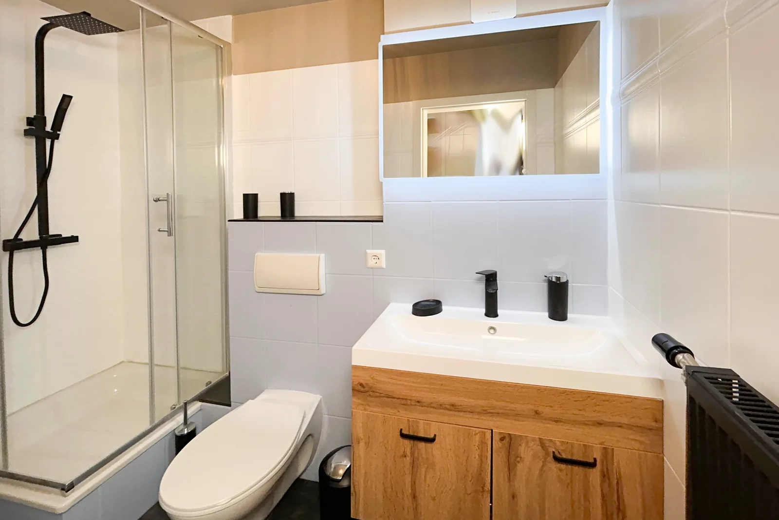 Badezimmer mit Holzwaschtisch, beleuchtetem Spiegel, WC und Glasdusche