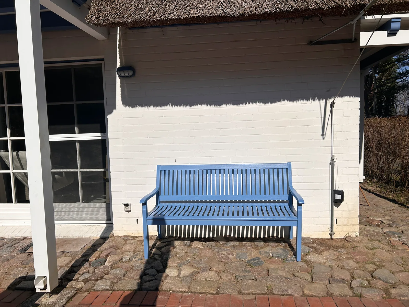 Blaue Gartenbank an der weißen Hauswand neben der Terrassentür